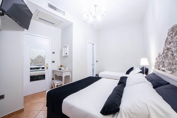 A hotel room with a bed, a desk, a chair, a television, and a chandelier.