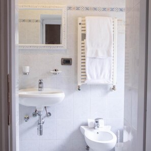 A bathroom with a sink, mirror, towel rack, and bidet.
