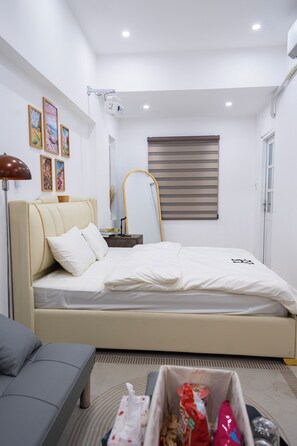 Quarto com cama, mesa de cabeceira, abajur e janela com persianas.