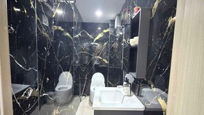 Un baño con pared de mármol, una bañera, un inodoro y un lavabo.