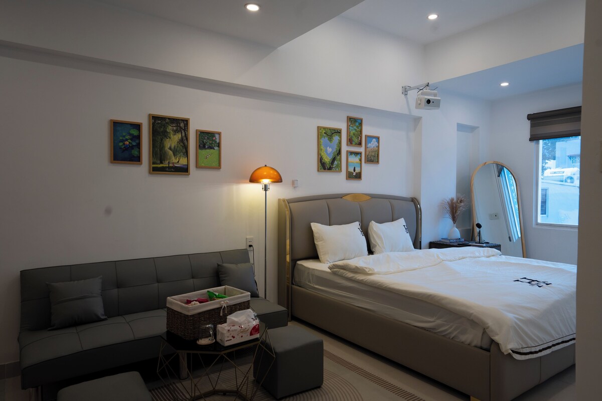 Quarto de hotel moderno com cama, sofá, mesinha e luminária.