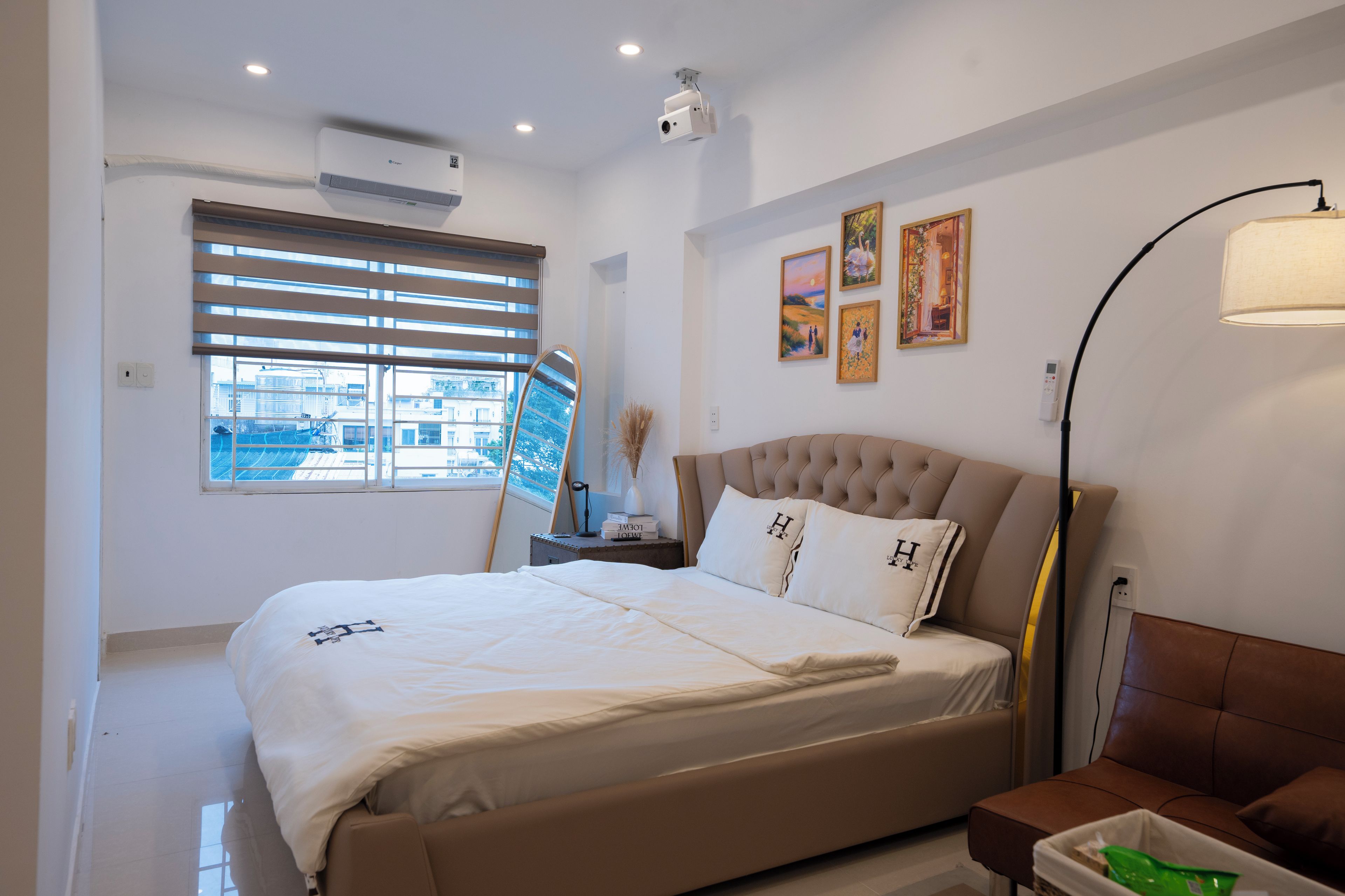 A hotel room with a bed, a bedside lamp, a window with blinds, and artwork on the wall.