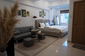 Quarto moderno com cama, sofá, mesa de centro e uma janela grande.
