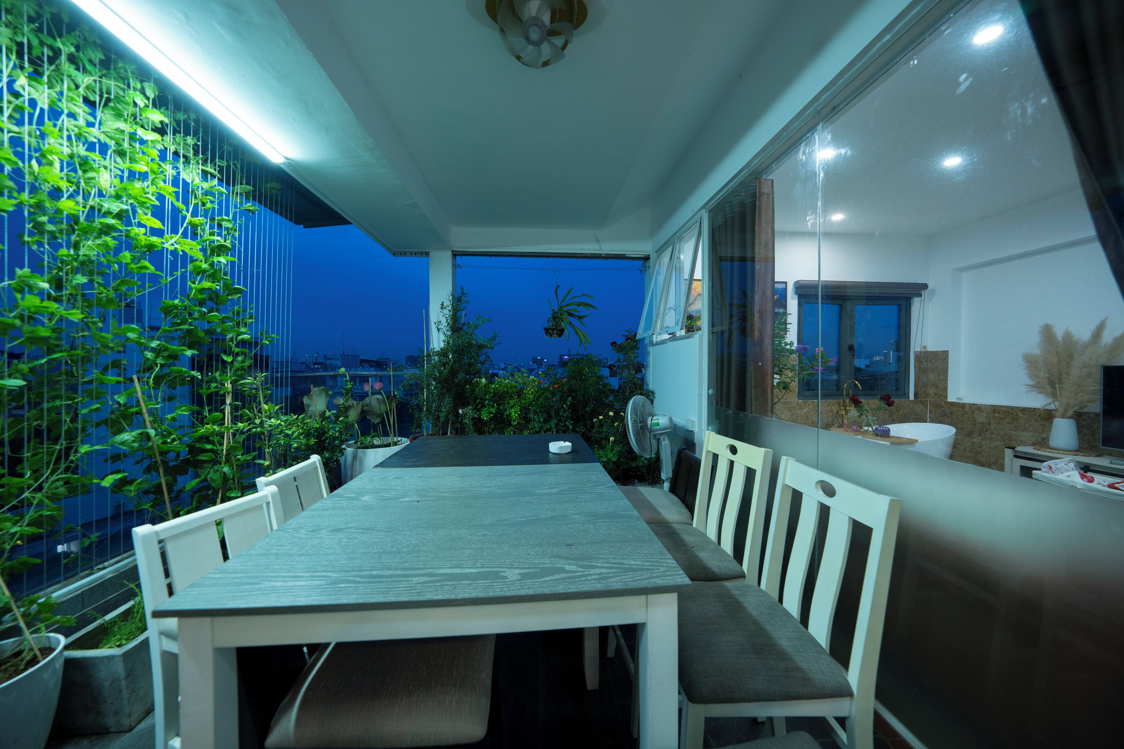 Un comedor con una mesa, sillas, un ventilador y vista a la ciudad al atardecer.