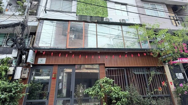 Un edificio de varios pisos con entrada al nivel de la calle, plantas en macetas y unidades de aire acondicionado visibles.