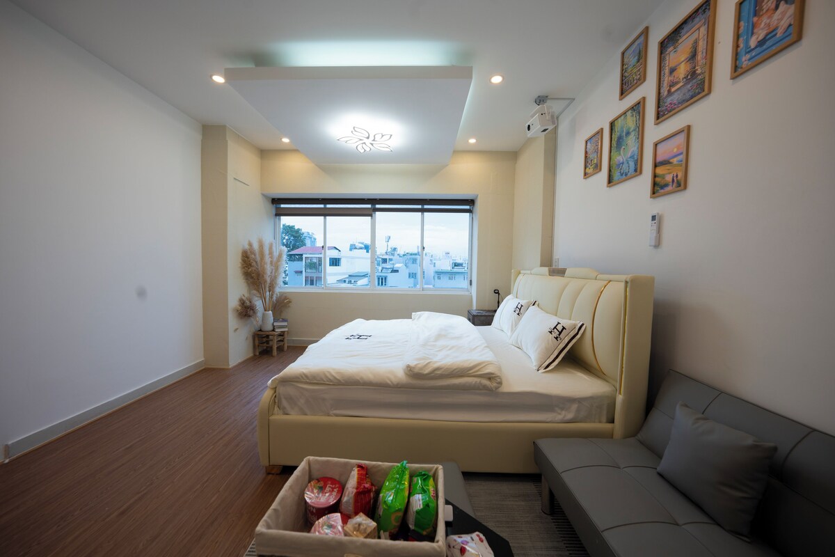 Quarto moderno com cama grande, sofá e janela com vista para a cidade.