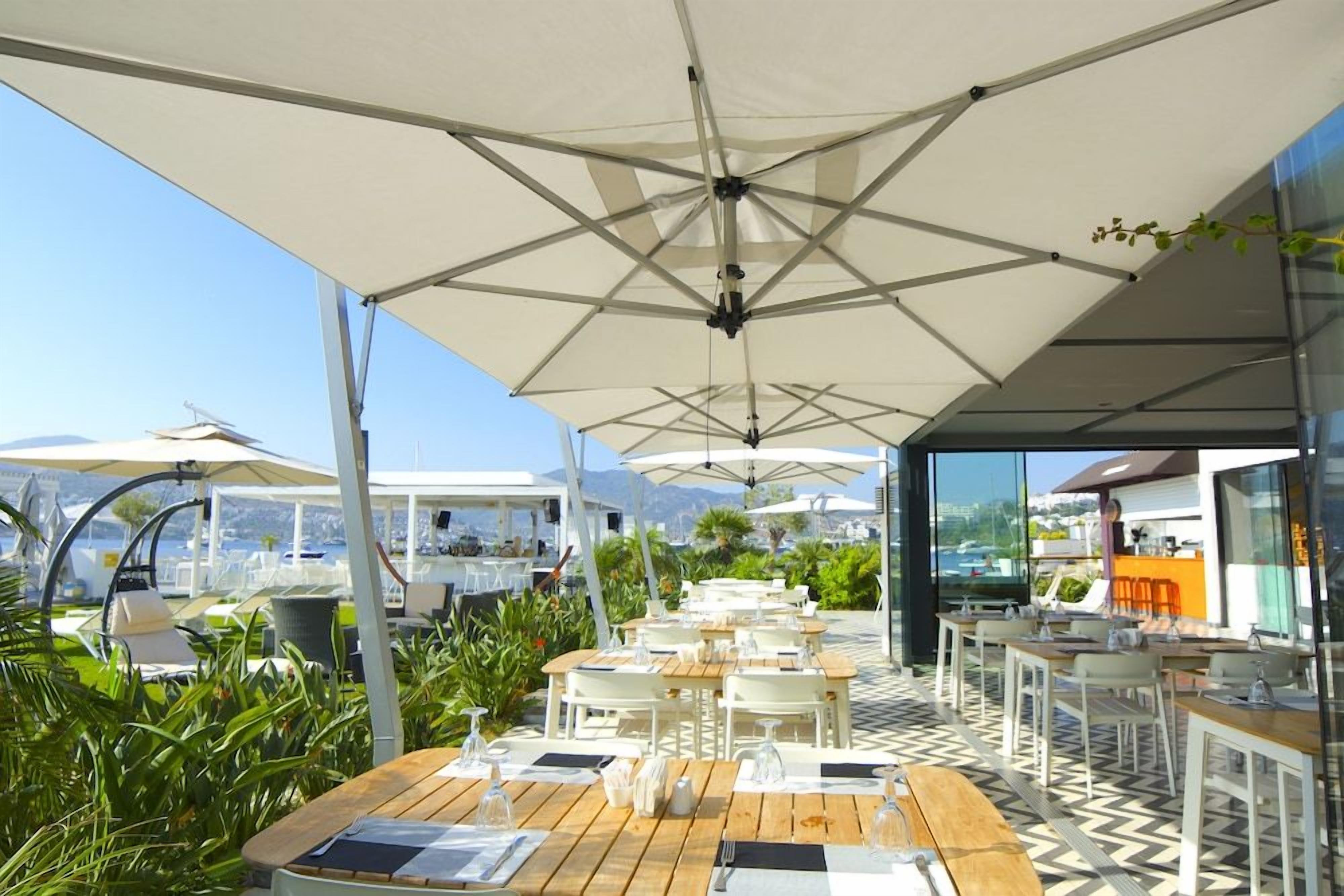 An outdoor dining area with tables and umbrellas, surrounded by greenery and overlooking a scenic view.