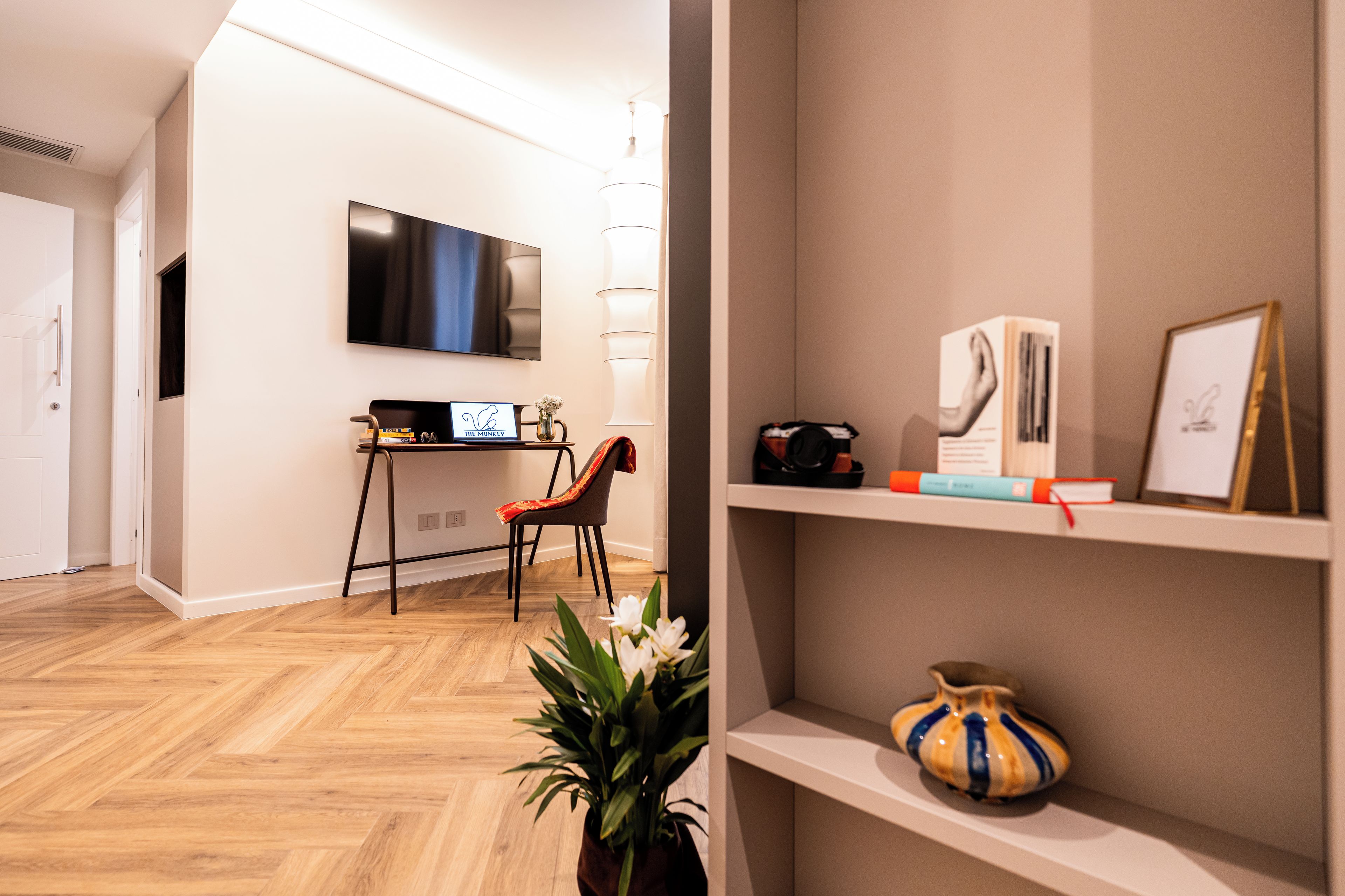 Uma sala de estar moderna com uma TV de tela plana na parede, piso de madeira e uma estante com livros e objetos decorativos.
