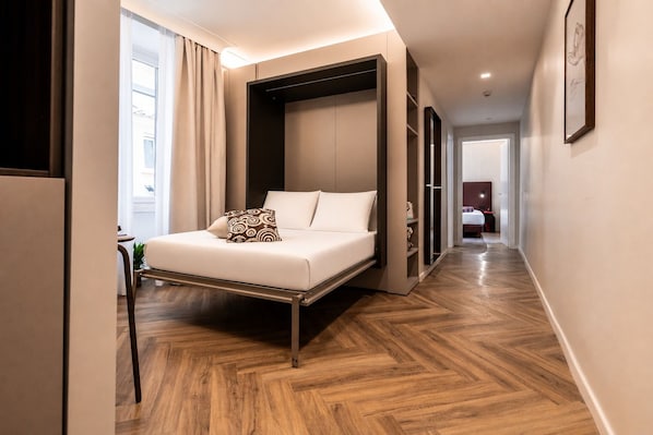 Une chambre d’hôtel moderne, équipée d’un lit, d’une armoire et d’un couloir menant à une autre pièce.