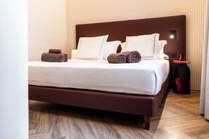 A neatly made bed with white linens and brown towels, a wooden headboard, and a bedside table with a book and a candle. - The Monkey Hotel  (Roma)