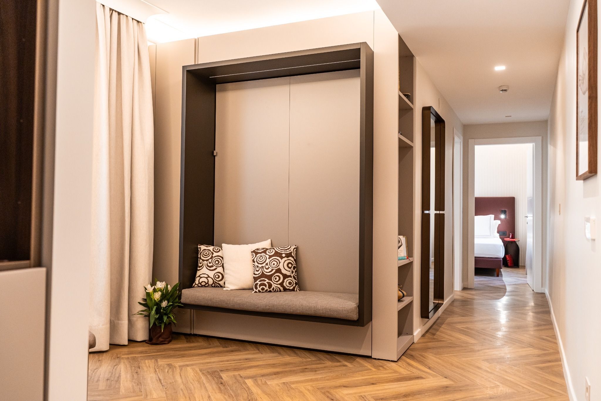 A modern hotel room with a built-in seating area, a potted plant, and a wooden floor.