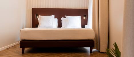 Un lit bien fait, avec une tête de lit en bois, une lampe de chevet et une plante en pot, dans une chambre d’hôtel.