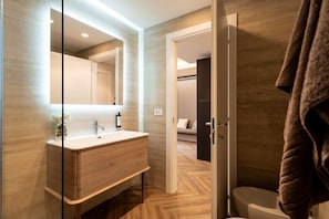 A modern bathroom with a wooden vanity, a glass shower enclosure, and a visible bedroom in the background. - The Monkey Hotel  (Roma)