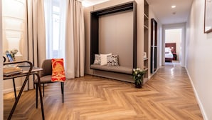 A modern living room with a sofa, a dining area with a laptop, and a hallway leading to a bedroom.