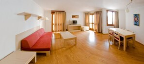 A room with a sofa, a small table, a TV on a stand, a dining table with chairs, and a painting on the wall. - Apartamentos Los Robles (Ibiza Town)