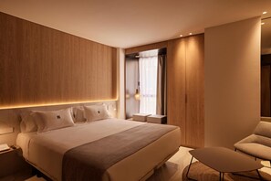 Habitació d'hotel moderna amb un llit gran, taules de nit, zona de seients i vistes a la ciutat.