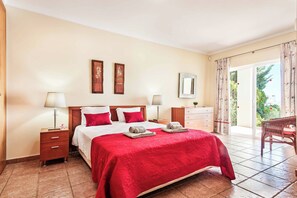 Ein Hotelzimmer mit einem Bett, zwei Nachttischen, einem Schminktisch, einem Schrank und einem Sessel, sowie einer Glastür zu einem Balkon.