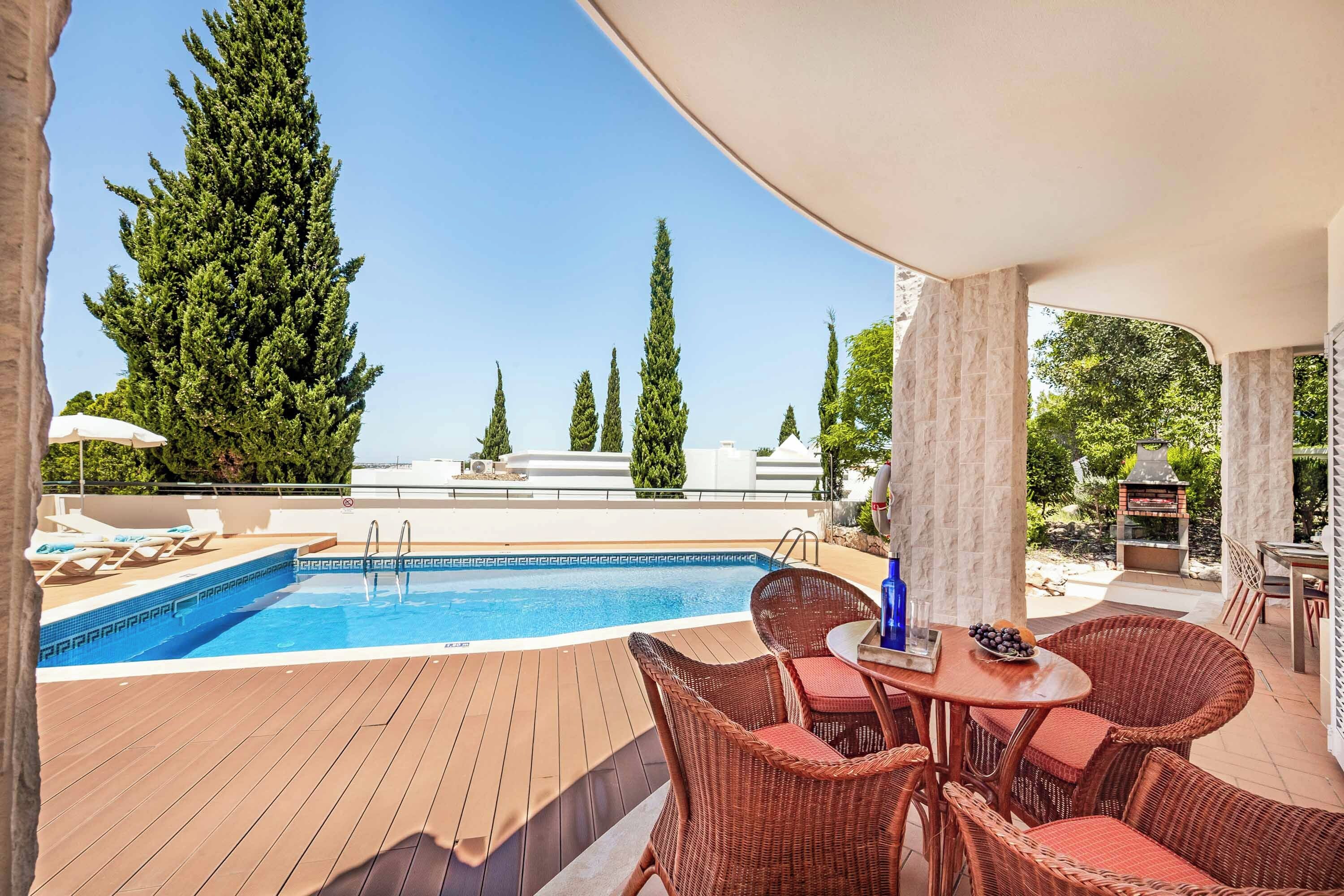 A rooftop pool area with a view of tall trees, a barbecue grill, and outdoor seating.