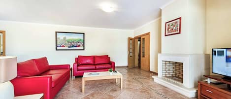 A living room with a red sofa, a coffee table, a fireplace, and a television.