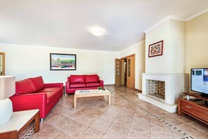Ein Wohnzimmer mit einem roten Sofa, einem Couchtisch, einem Kamin und einem Fernseher.
