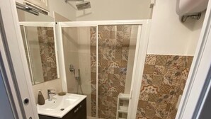 Baño pequeño con ducha, inodoro y lavamanos.