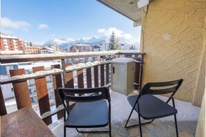 Ein Balkon mit zwei Stühlen und Blick auf schneebedeckte Berge sowie Gebäude im Hintergrund.