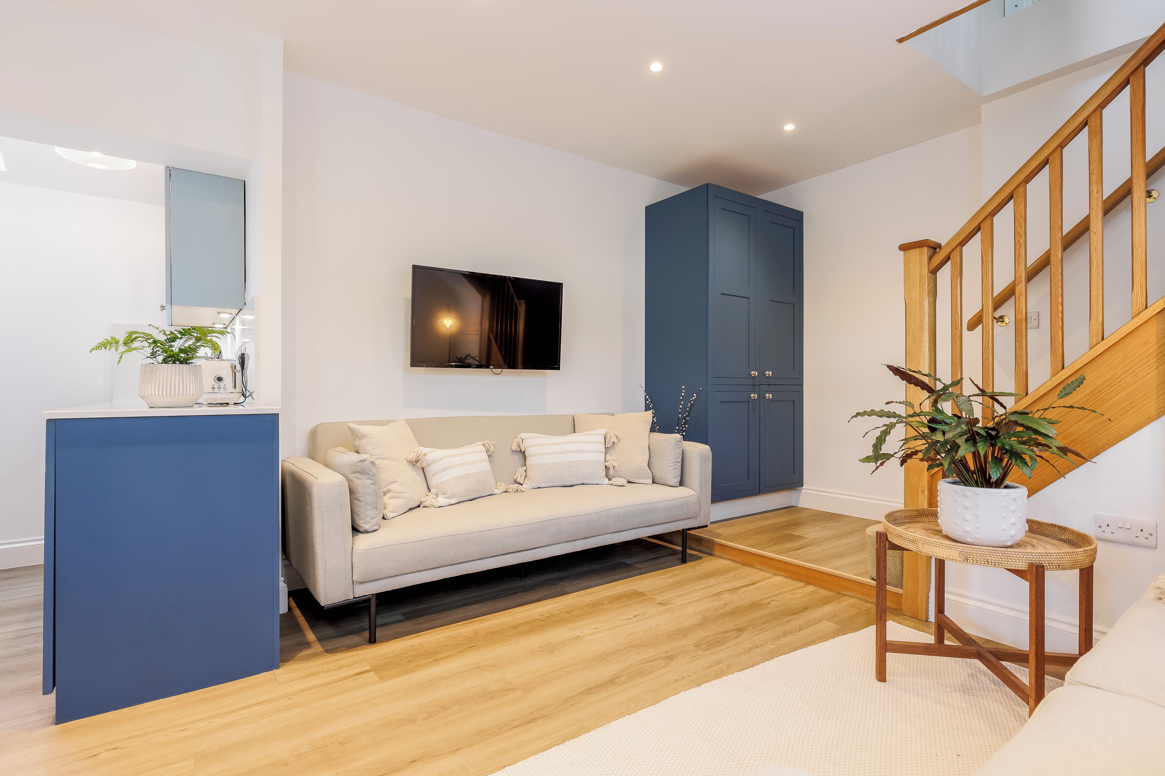 A modern living room with a sofa, a television, a cabinet, and a staircase.