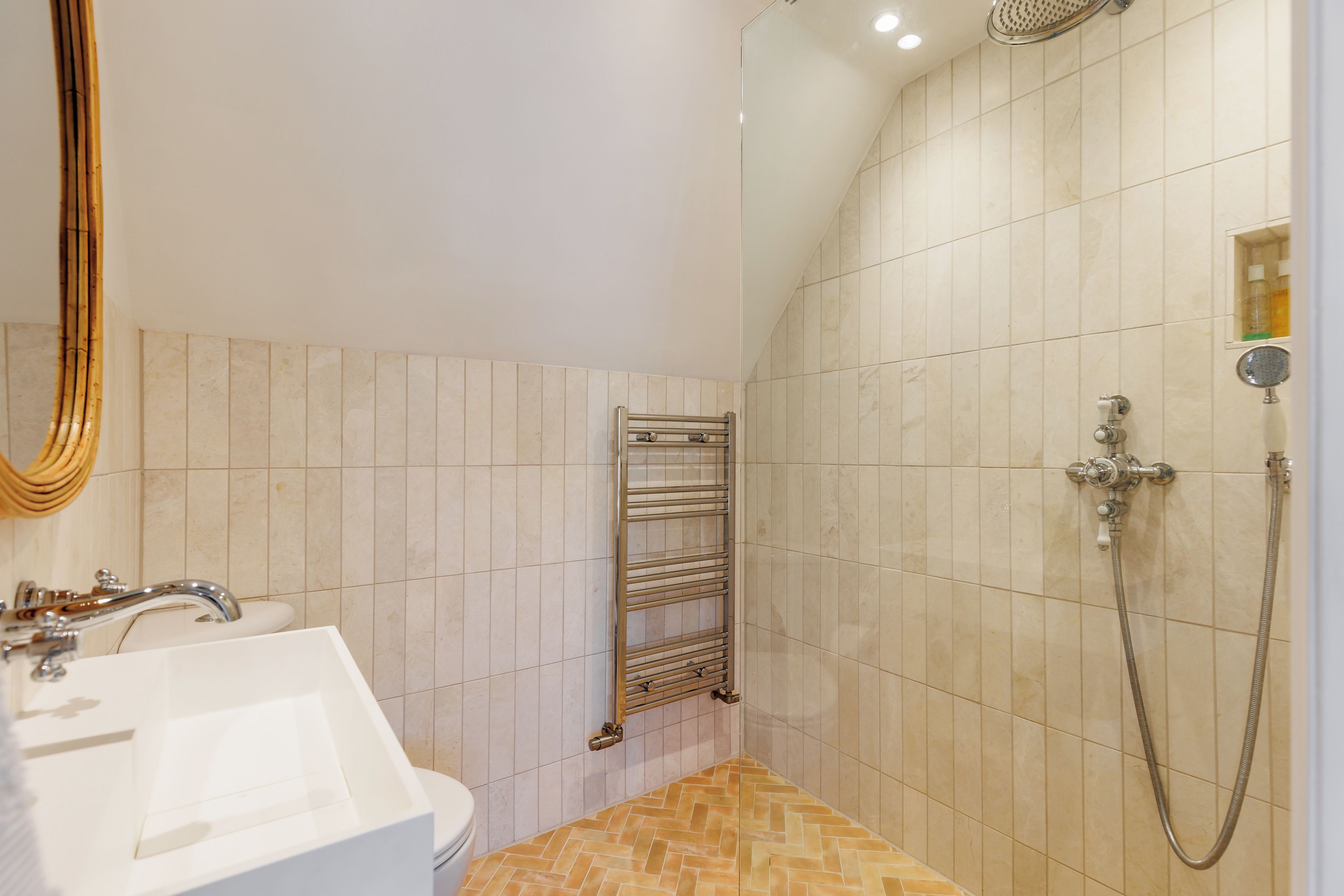 Ein Badezimmer mit einem weißen Waschbecken, einem Spiegel, einer Dusche inklusive Handbrause und einem Handtuchhalter.