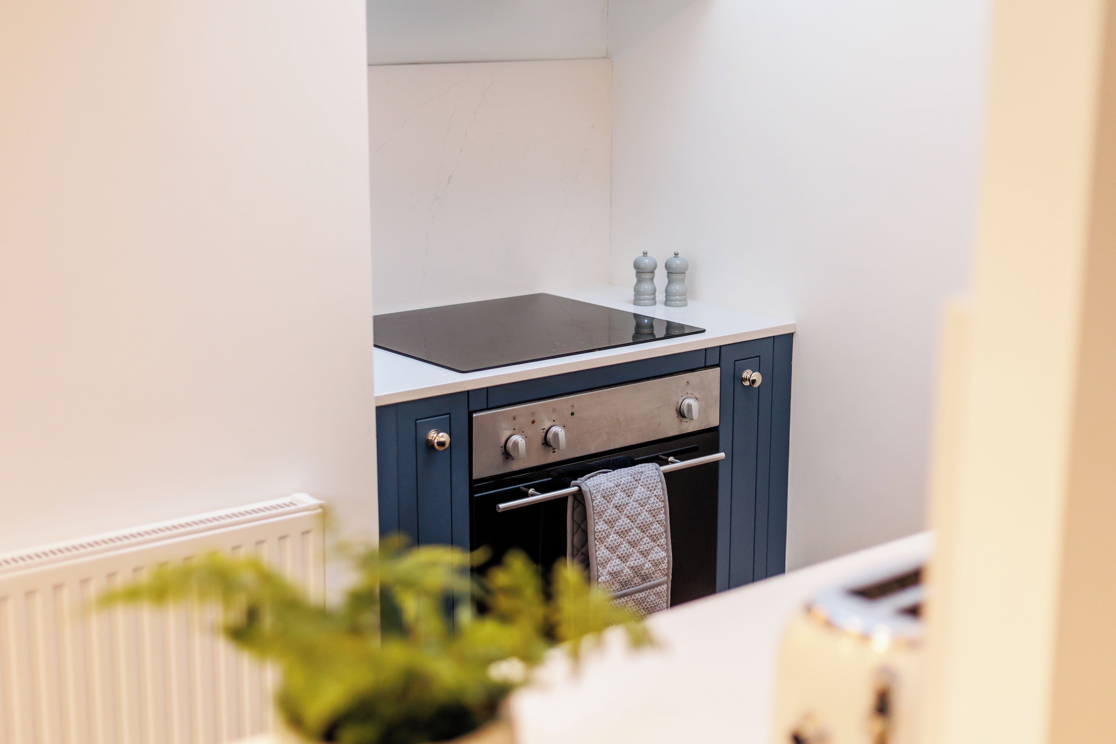 Une cuisine compacte avec une plaque de cuisson noire, un four encastré et un plan de travail blanc.