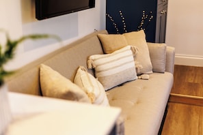A beige sofa with multiple cushions, a television mounted on the wall, and a decorative plant in the foreground.