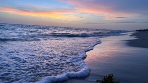 Uma praia com ondas se aproximando da costa, céu claro e horizonte distante.