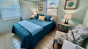 Ein Schlafzimmer mit einem Bett, Nachttischen, einem Sessel und einem Fenster.