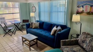 Ein Wohnzimmer mit einem blauen Sofa, einem gemusterten Sessel, einem kleinen Tisch und einer Lampe.