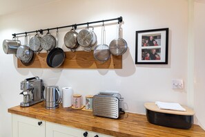 A kitchen with a wooden countertop, a coffee maker, a kettle, a toaster, and a hanging pot rack. - Cozy 2Bed Flat with Private Patio, Shepherd’s Bush - Pass the Keys (London)