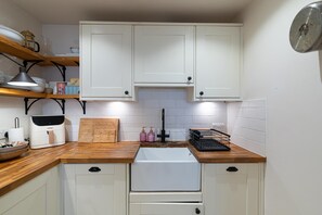 A compact kitchen with white cabinets, a wooden countertop, a coffee maker, and a sink. - Cozy 2Bed Flat with Private Patio, Shepherd’s Bush - Pass the Keys (London)