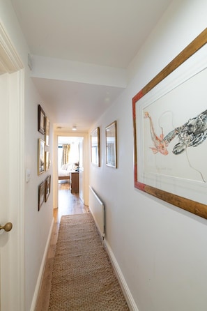 A hallway with framed artwork on the walls, a wooden door, and a carpeted floor. - Cozy 2Bed Flat with Private Patio, Shepherd’s Bush - Pass the Keys (London)