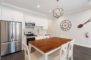 A modern kitchen with stainless steel appliances, white cabinetry, a wooden dining table, and a decorative wall clock. - Vibrant NOLA Home for Large Groups (New Orleans)