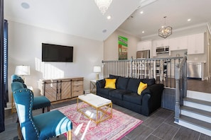 A modern living room with a black sofa, a blue armchair, a coffee table, and a TV. - Vibrant NOLA Home for Large Groups (New Orleans)