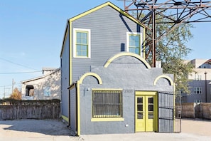 A two-story building with a yellow door and a window with a metal grill. - Vibrant NOLA Home for Large Groups (New Orleans)