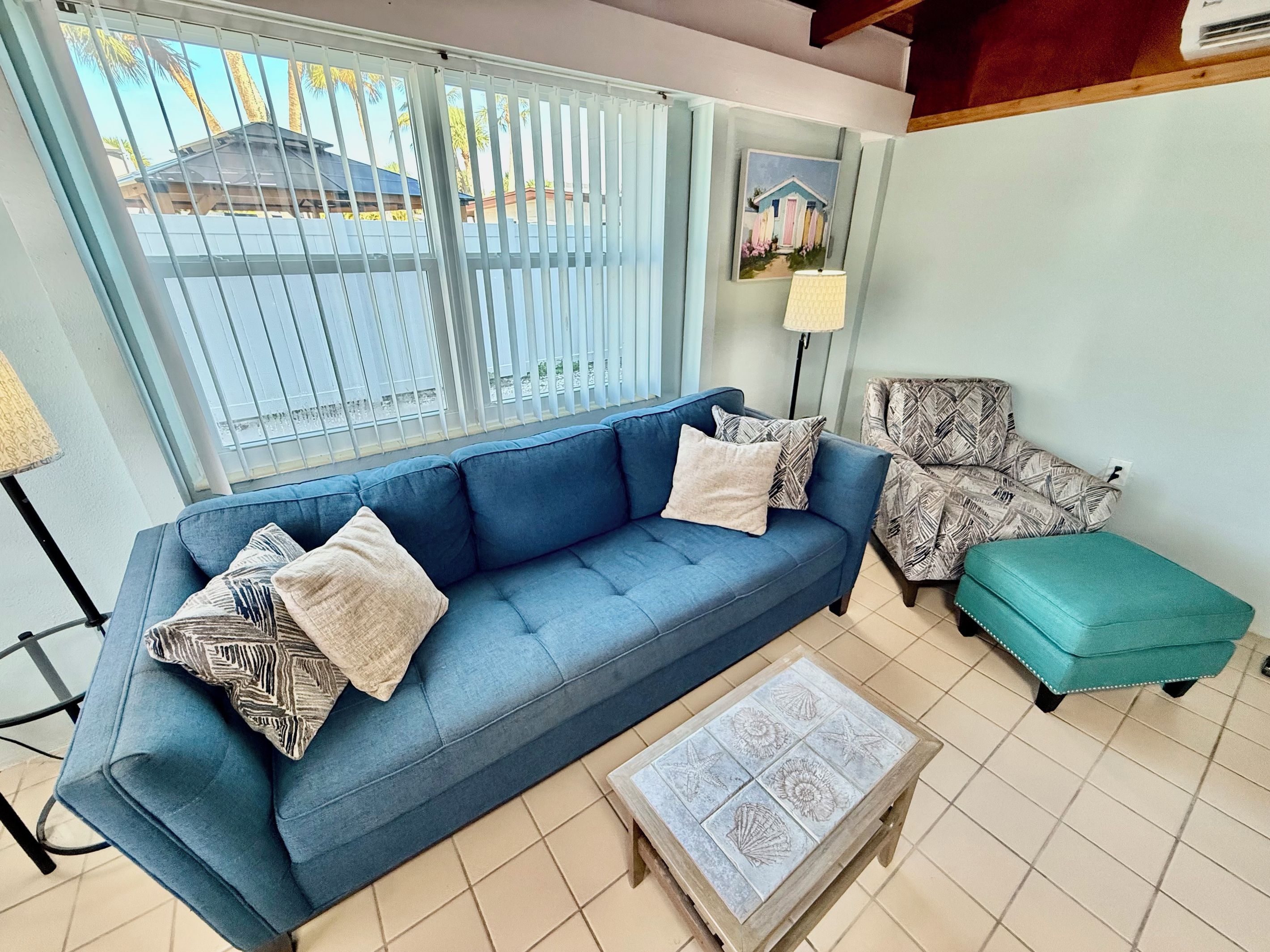 A living room with a blue sofa, patterned armchair, teal ottoman, and a small table with a decorative tile top.