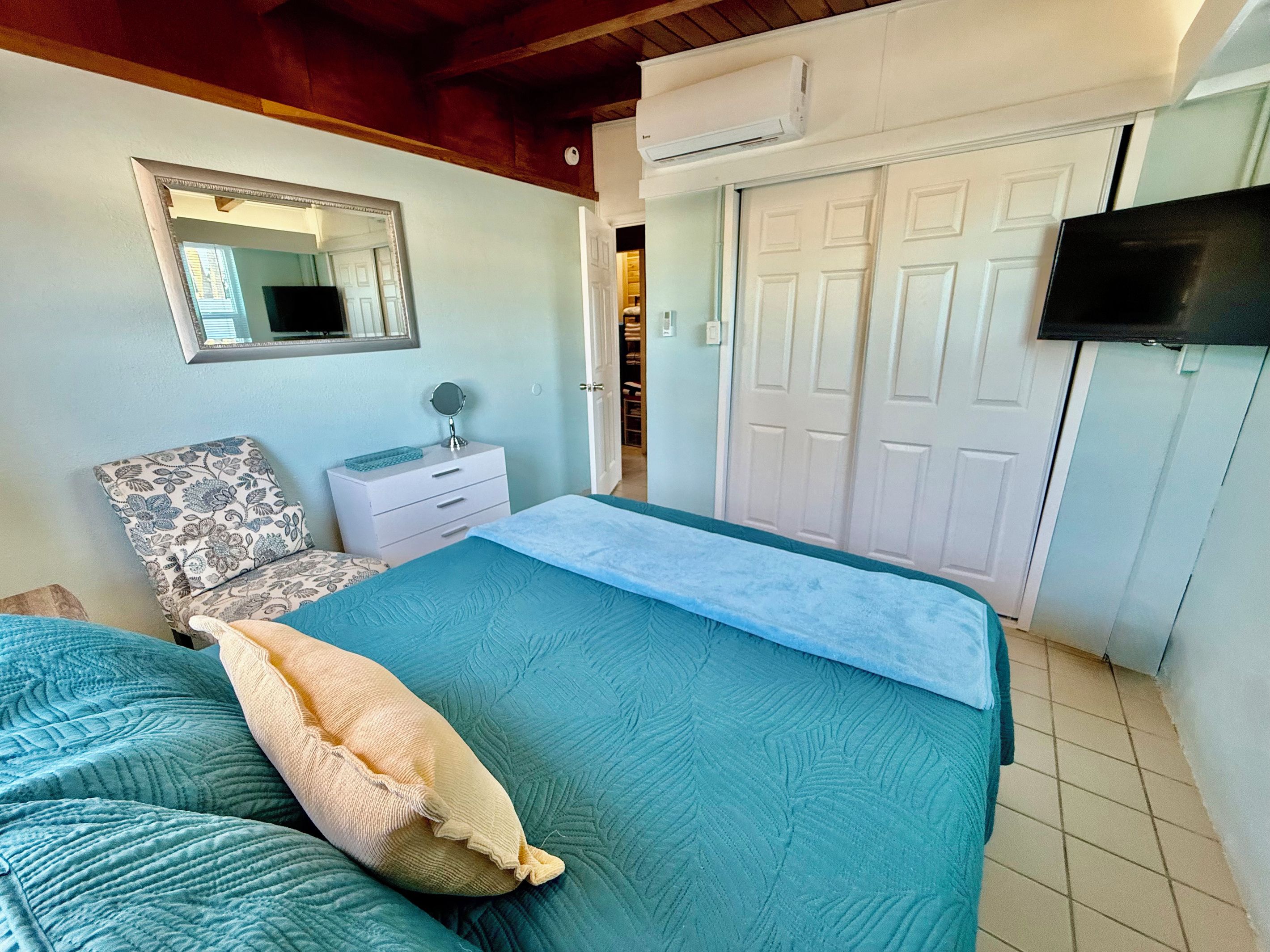 A bedroom with a bed, a nightstand, a mirror, a wardrobe, and a television.
