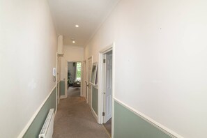 A narrow hallway with white walls and green trim, leading to a room with a door and a window. - A Comfortable Home in the Heart of Ealing - Pass the Keys (London)