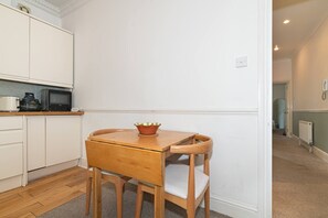 A compact kitchen with white cabinetry, a wooden table with a bowl, and a chair. - A Comfortable Home in the Heart of Ealing - Pass the Keys (London)