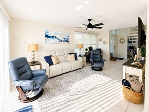 Ein Wohnzimmer mit einer Couch, einem Relaxsessel, einem Couchtisch, einem Fernseher und einem Deckenventilator.