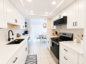 Cozinha moderna com armários brancos, fogão preto e área de refeições com mesa e cadeiras brancas.