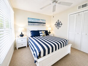Ein Schlafzimmer mit einem Bett, Nachttischen, einem Deckenventilator, einer Kompass-Wanddekoration und einem Fenster mit Jalousien.