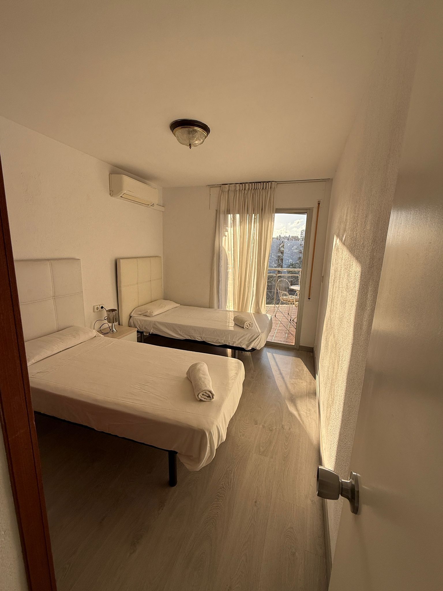 A hotel room with two beds, a window with curtains, a ceiling light, and a view of the outside.