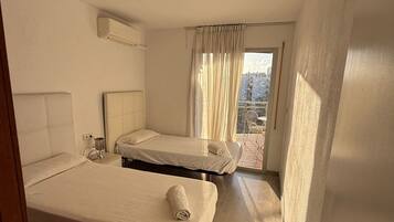 A hotel room with two beds, a window with curtains, a ceiling light, and a view of the outside.