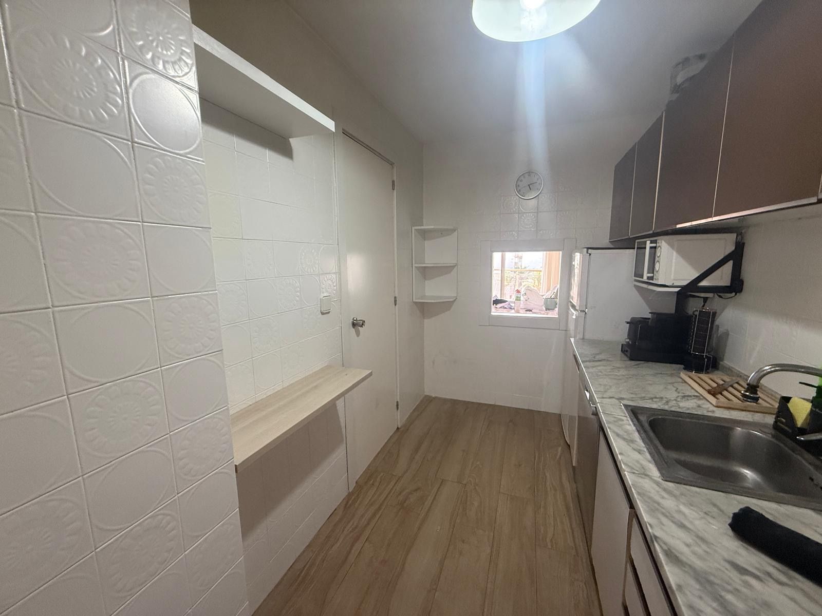 A kitchen with white tiles, a wooden floor, a window, and a microwave.