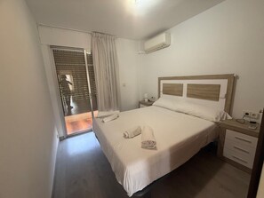 A hotel room with a bed, a nightstand, a bedside table, an air conditioning unit, and a sliding glass door leading to an outdoor area. - Salou at Your Feet | Beach, Views, and Relaxation (Salou)